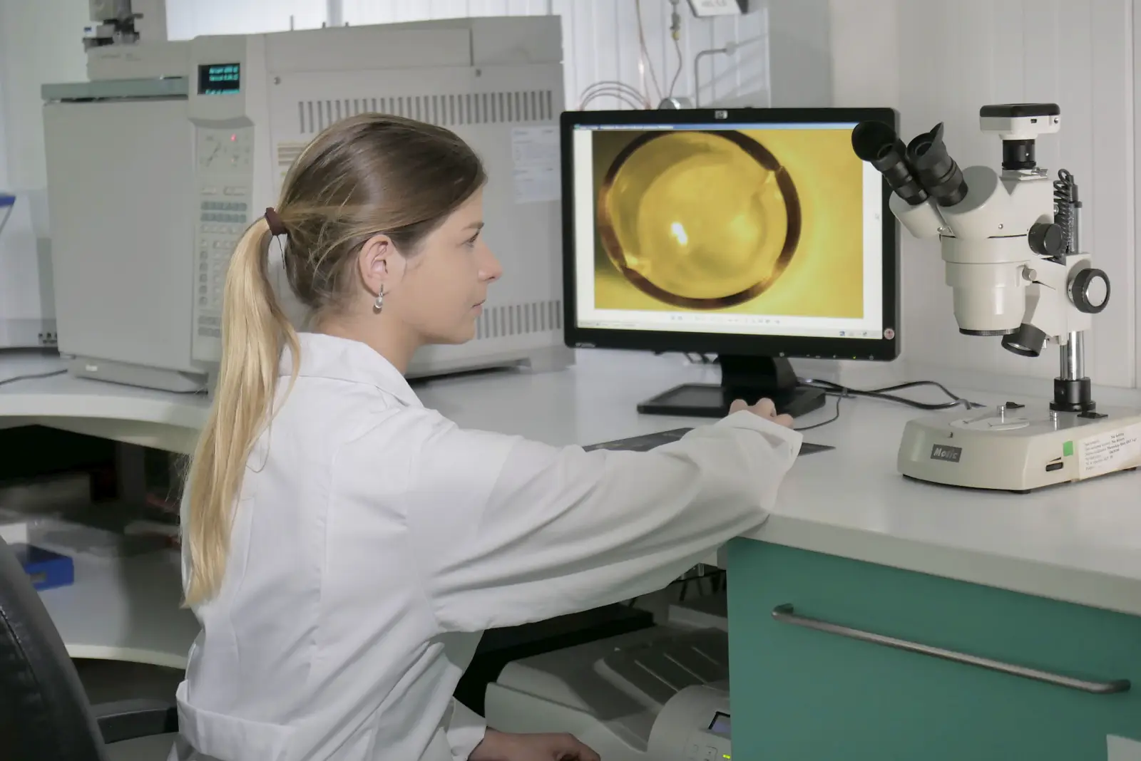 Pracownica laboratorium przy mikroskopie, na ekranie przekrój kapsułki
